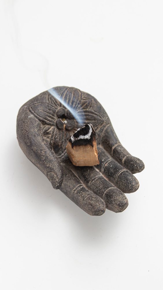 An indian inspired metal sculpture of a palm holding stick of smoking incense