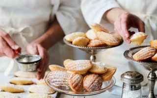 Two chefs prepare and dust dishes of madeleines with sugar