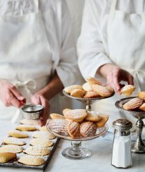 Two chefs prepare and dust dishes of madeleines with sugar