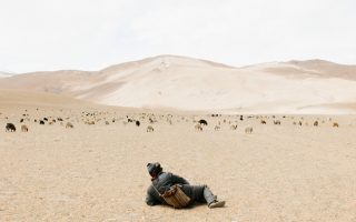 Young Kashmirin boy lies in a dessert looking at mountains