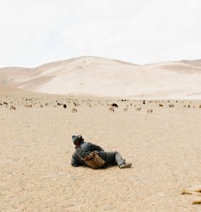 Young Kashmirin boy lies in a dessert looking at mountains