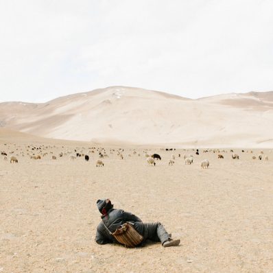 Young Kashmirin boy lies in a dessert looking at mountains