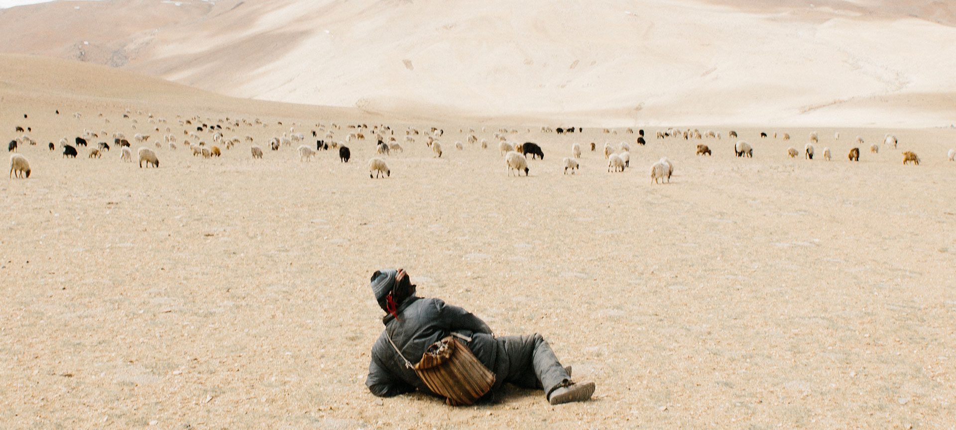 Young Kashmirin boy lies in a dessert looking at mountains