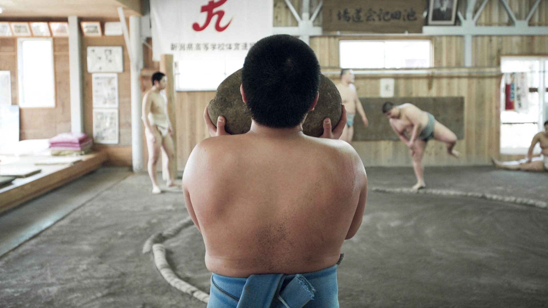 A young Japanese sumo carries a heavy weighted rock
