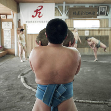 A young Japanese sumo carries a heavy weighted rock