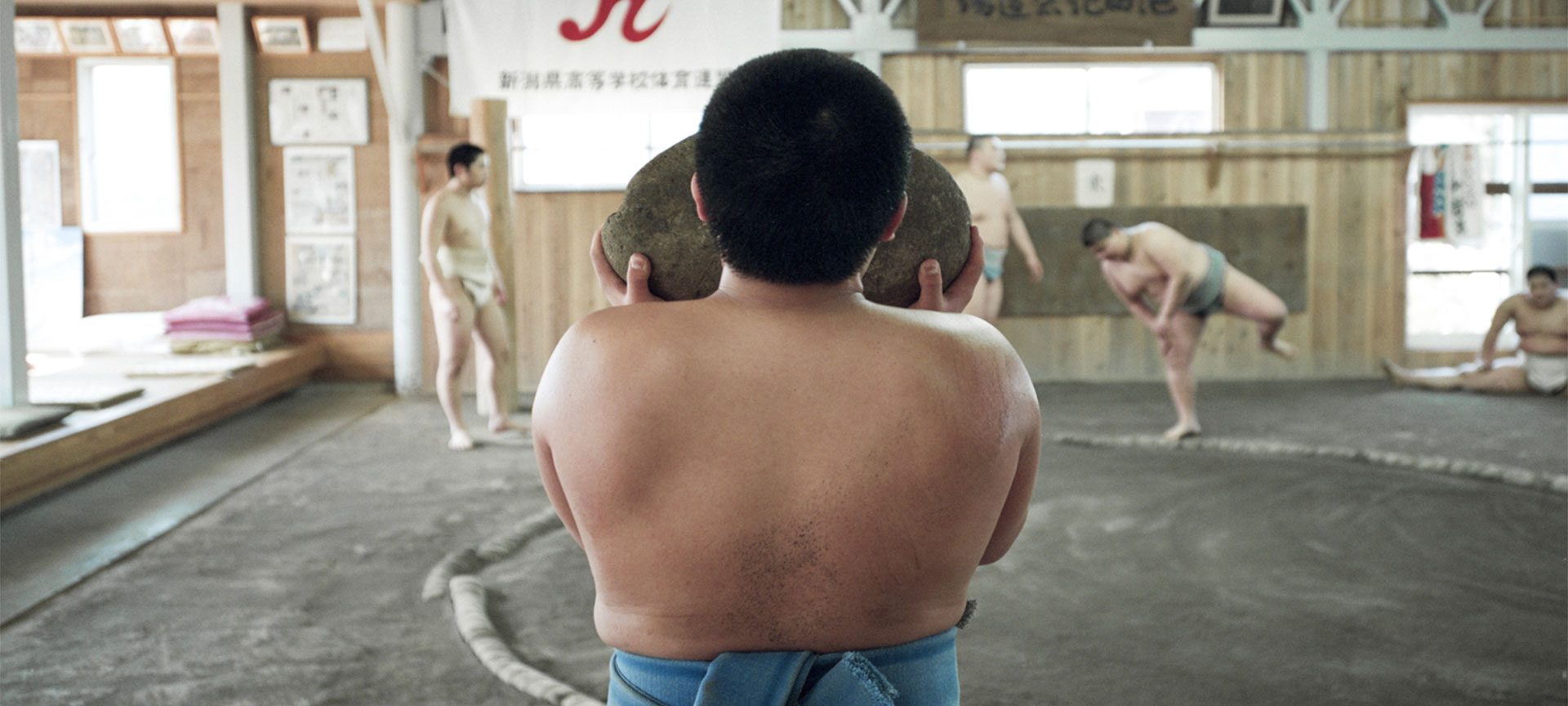 A young Japanese sumo carries a heavy weighted rock